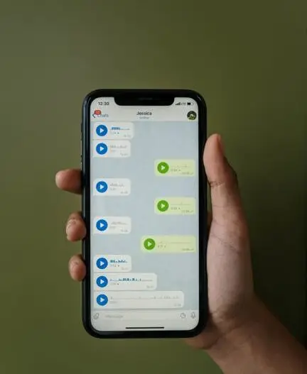 Close-up of a smartphone displaying a messaging app with voice messages in a hand.